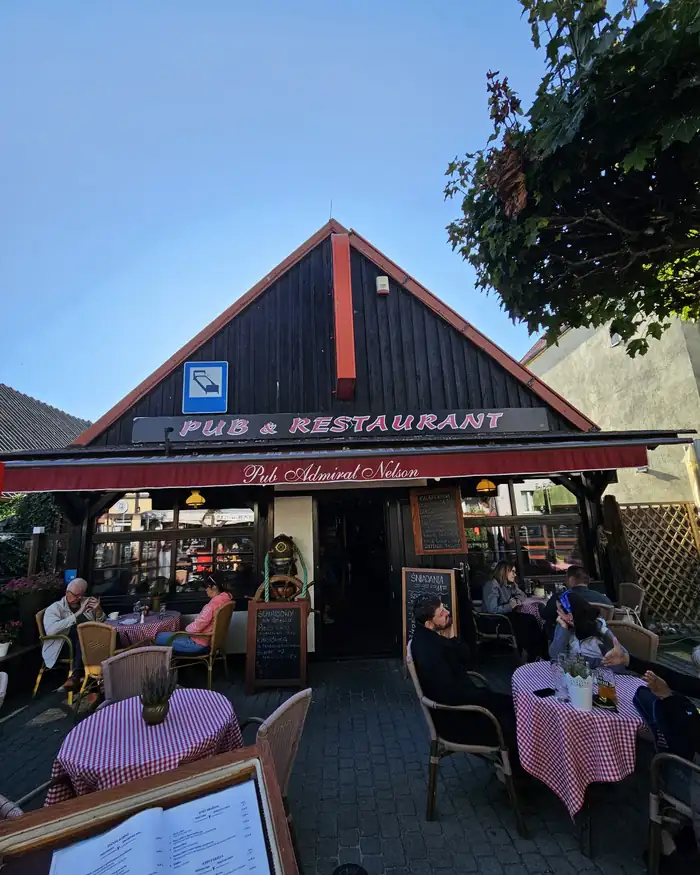 Drewniany szczyt z napisem Pub & Restaurant i stoliki z różowymi obrusami