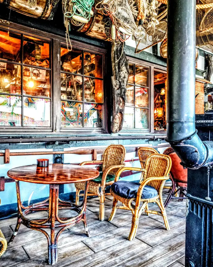 Taras z okrągłym stolikiem i wiklinowymi krzesłami przy podświetlonych oknach